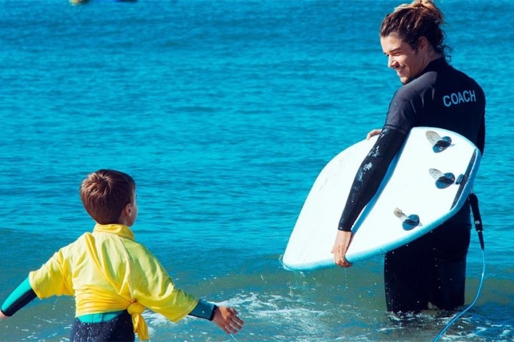 a young man carrying a surf board on a body of water