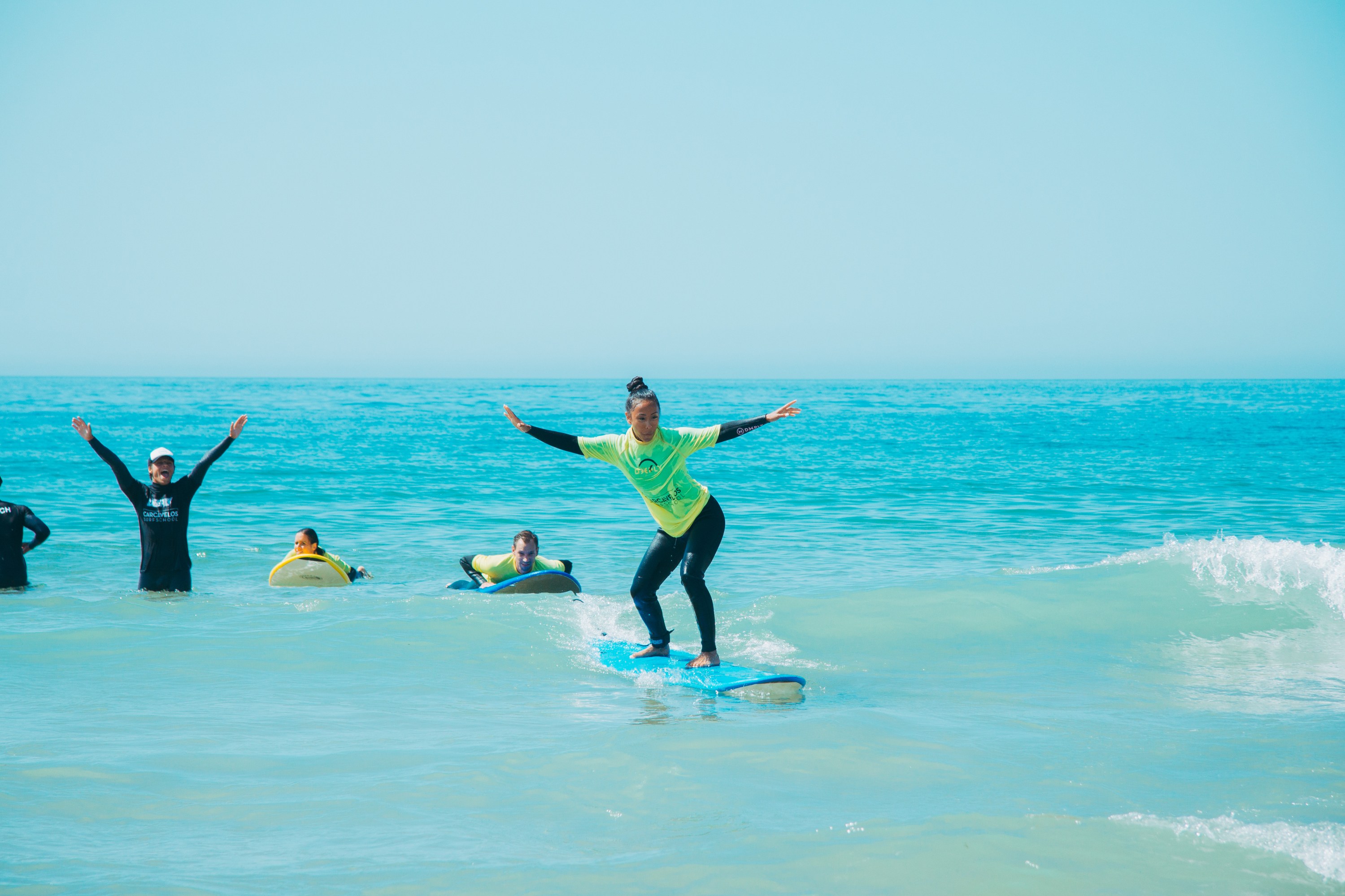 Person surfing on small wave with others watching in the ocean.