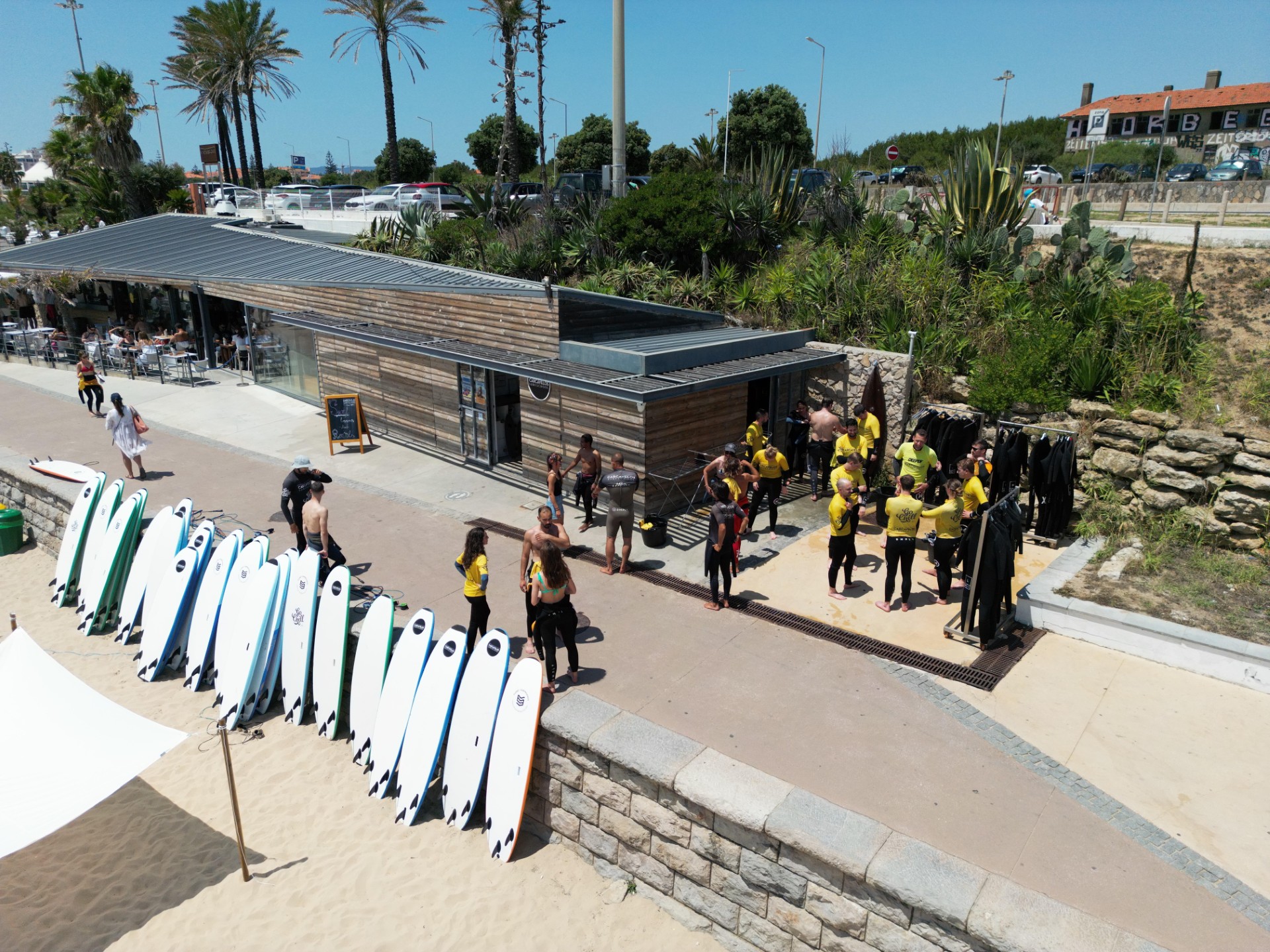 Group of surfers in yellow shirts gather near surfboards at a beachside shack.